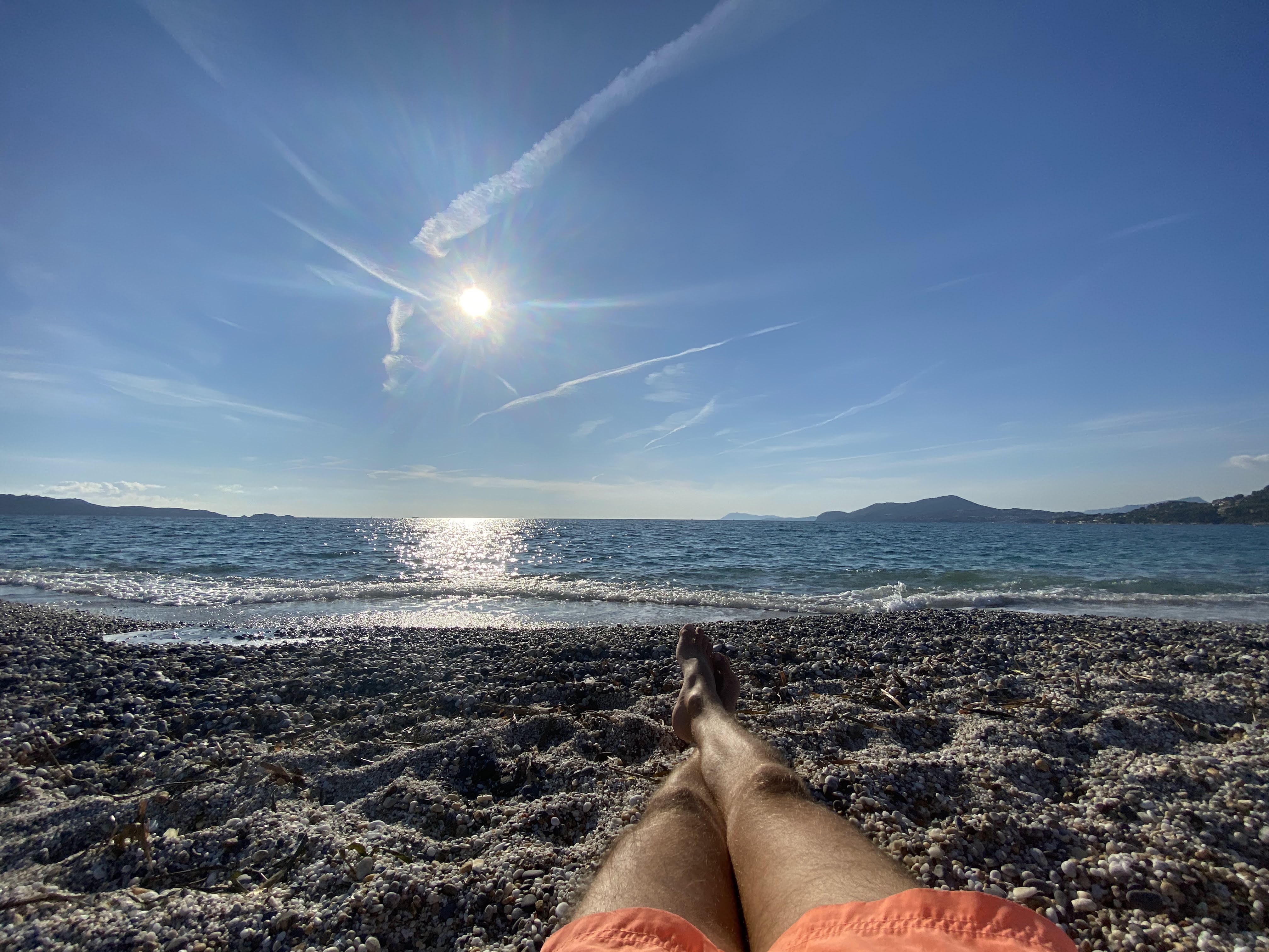 Vue sur la mer depuis une plage de galets à Hyères, avec le soleil au-dessus de l’eau