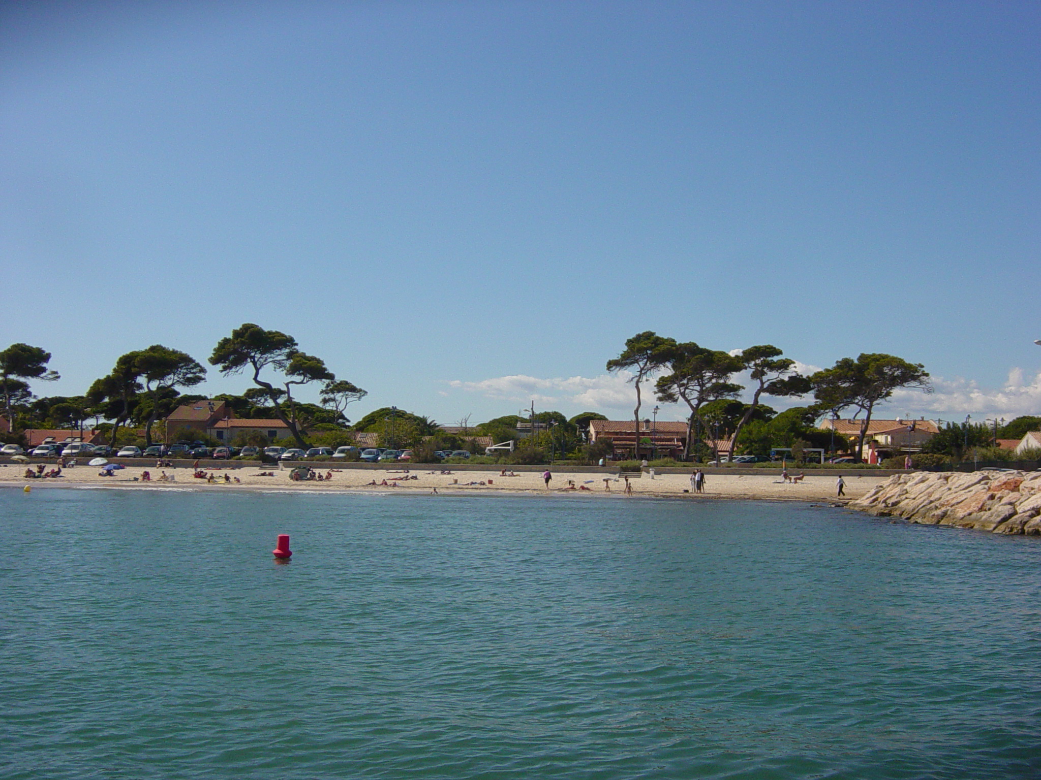 Vue de la plage de La Capte depuis la mer, avec pins parasols et maisons du village